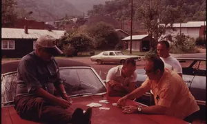 Miners playing cards on the hood of a car during the Brookside Mine strike in Harlan County, Kentucky, 1974. The mine is visible in the background.